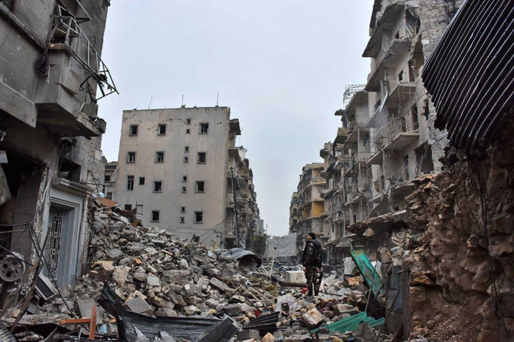 Seorang anggota pasukan pemerintah Suriah berdiri di dekat bangunan-bangunan yang hancur akibat peperangan di lingkungan Al-Kalasseh, Aleppo.