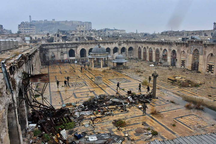 Pasukan pro pemerintah Suriah berjalan di dekat masjid kuno Umayyah, dengan latar depan kota tua Aleppo dan latar belakang benteng kota.