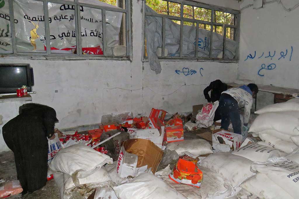Warga sipil Suriah mengambil makanan dari ruang penyimpanan yang sebelumnya dipegang oleh pasukan oposisi di lingkungan al-Kalasseh, Aleppo timur.