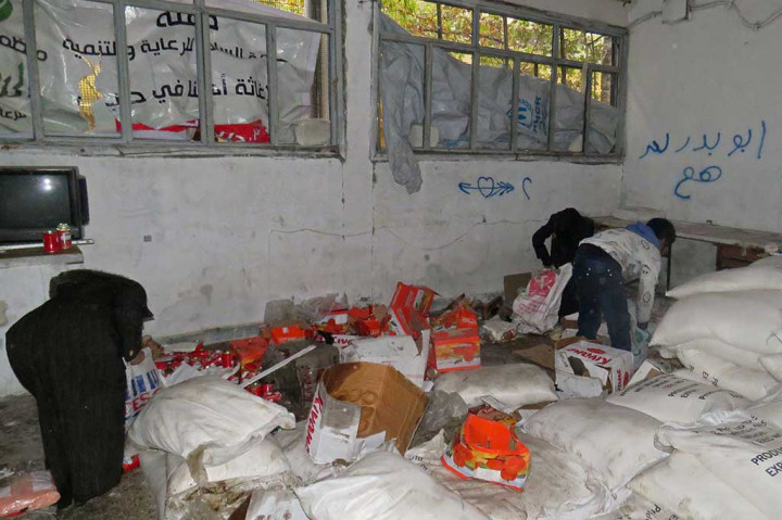 Warga sipil Suriah mengambil makanan dari ruang penyimpanan yang sebelumnya dipegang oleh pasukan oposisi di lingkungan al-Kalasseh, Aleppo timur.