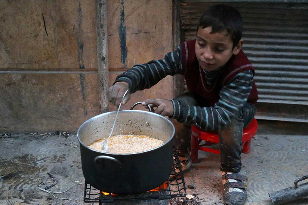 Seorang anak memasak di jalanan di daerah yang dikuasai pemberontak di Aleppo, selama operasi pasukan pemerintah Suriah untuk merebut kembali kota tersebut.