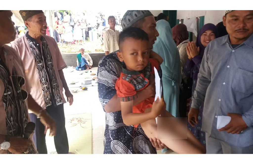 Seorang bapak menggendong anaknya yang akan di sunat.