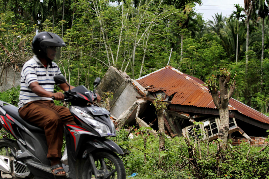 Pengendara sepeda motor melintas di rumah yang roboh akibat gempa 6,5 SR di Kecamatan Bandar Baru, Pide Jaya, Aceh.