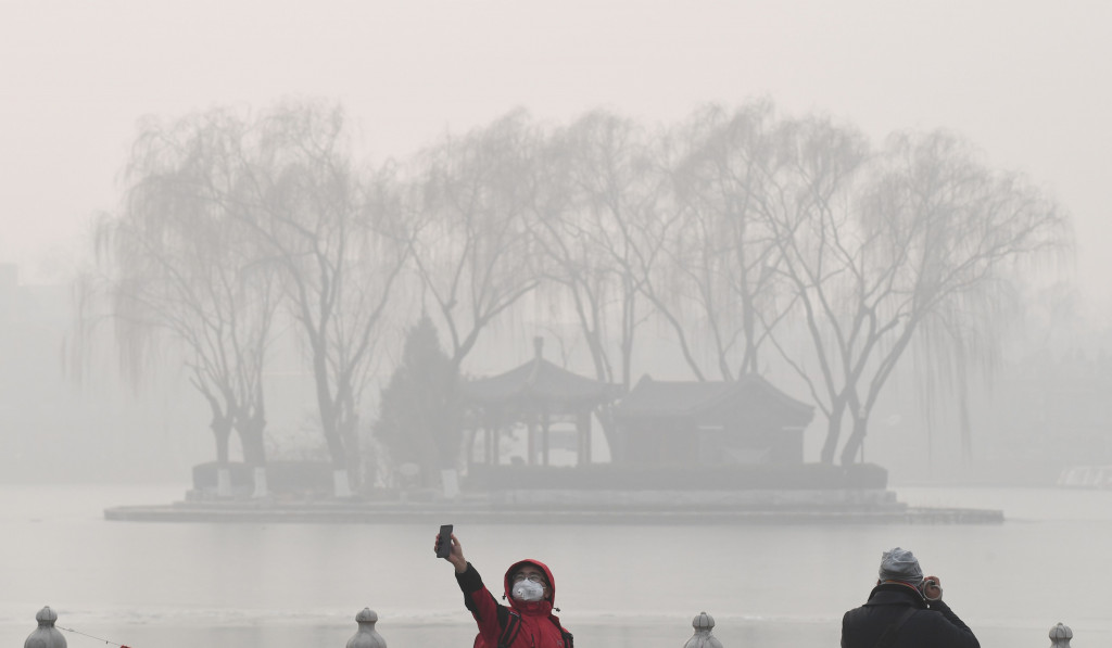 Seorang warga sedang selfie dengan latar belakang danau di Beijing yang nyaris tidak terlihat akibat tertutup kabut polusi udara. AFP Photo/GREG BAKER