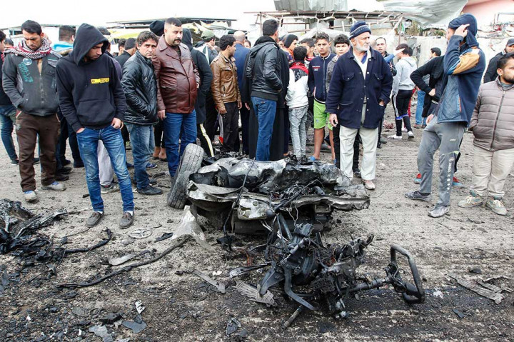 Warga berkerumun di dekat mobil yang hancur akibat serangan bom di Kota Sadr.