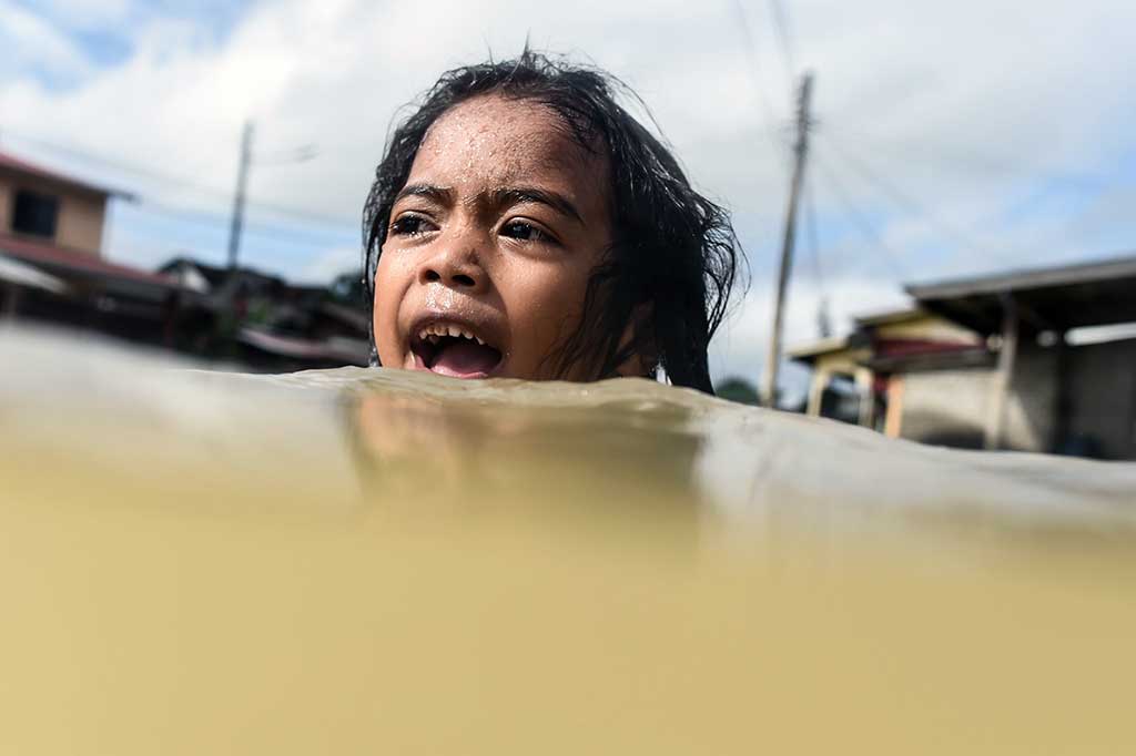 Seorang anak berenang di depan rumahnya yang dilanda banjir di Rantau Panjang, Kelantan, wilayah Malaysia yang berbatasan dengan Thailand, Kamis.