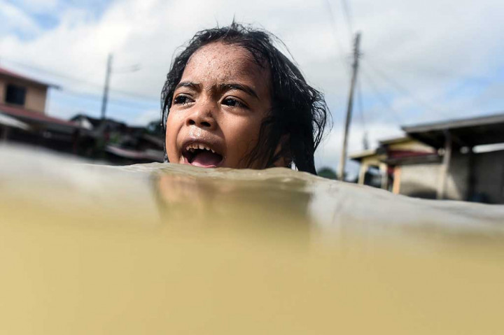 Seorang anak berenang di depan rumahnya yang dilanda banjir di Rantau Panjang, Kelantan, wilayah Malaysia yang berbatasan dengan Thailand, Kamis.