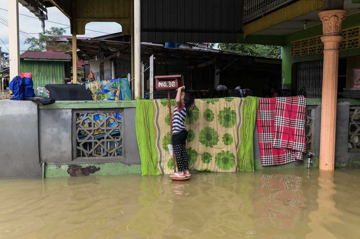 Seorang anak berdiri di dekat kotak surat di depan rumahnya yang terandam banjir di Rantau Panjang, Kelantan.