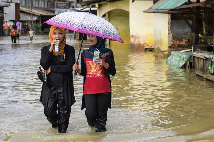 Dua remaja putri melintasi banjir yang melanda wilayah Rantau Panjang, Kelantan.