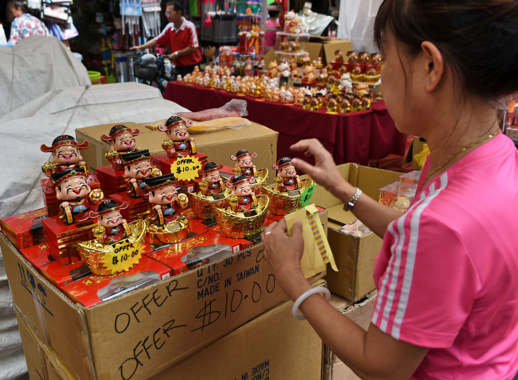 Seorang wanita pedagang kaki lima di China Town membersihan boneka Dewa Keberuntungan yang biasanya banyak diburu warga. 