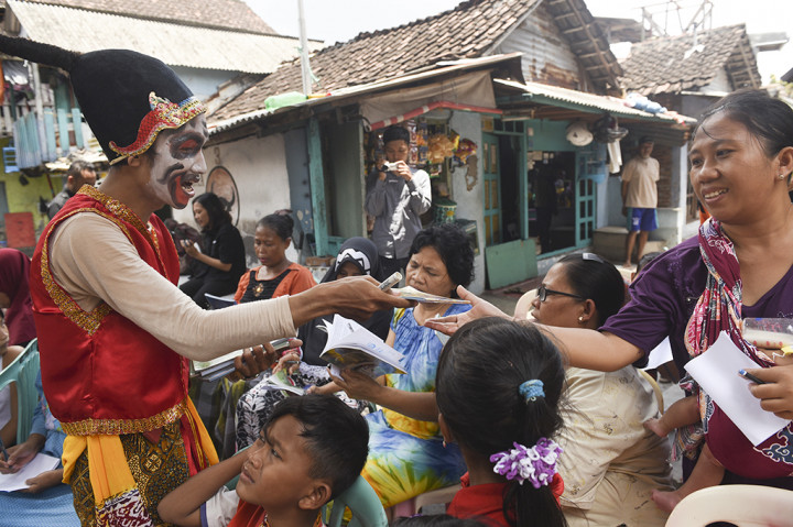 Haris Rizki dengan mengenakan kostum tokoh wayang petruk membagikan buku ke warga ketika dia mengajar di kampung Tambak Asri, Surabaya, Jawa Timur.