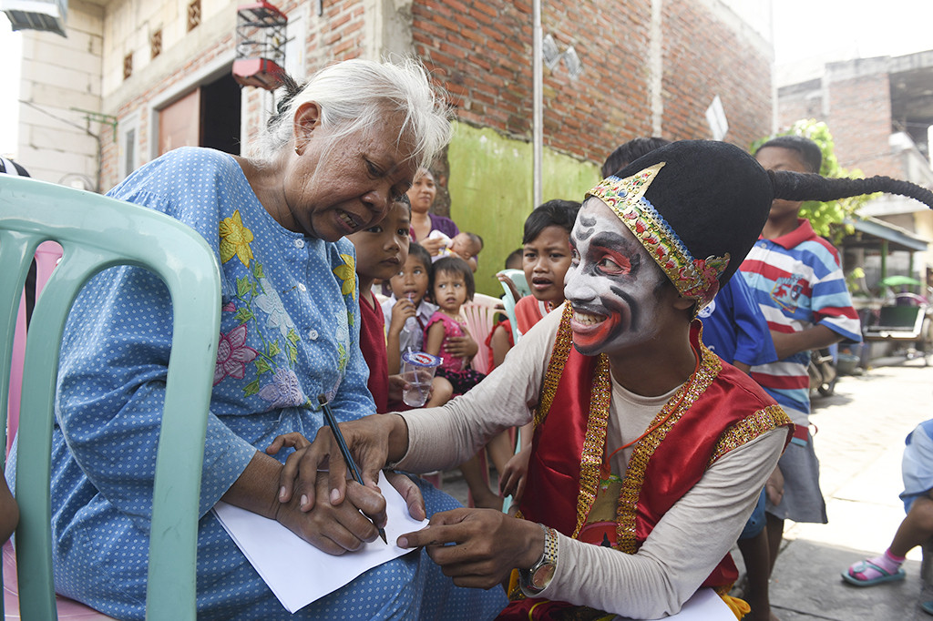 Haris Rizki dengan  mengenakan kostum petruk membantu seorang ibu menulis.