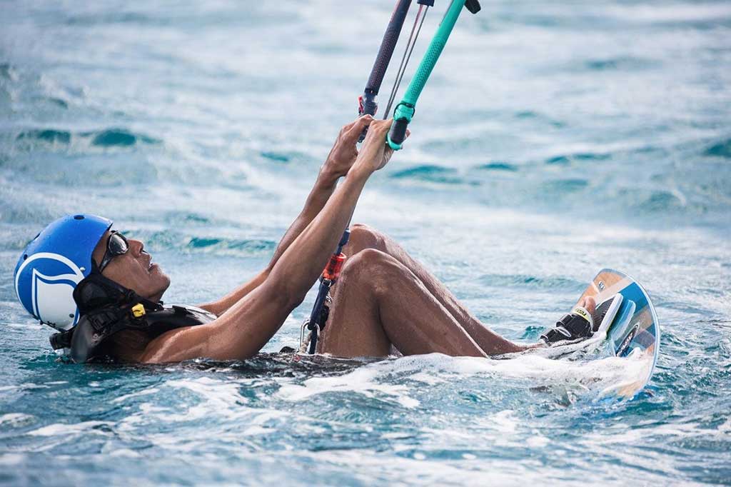 Obama tersenyum di papan speed boat dengan mengenakan helm dan kacamata saat ia mencoba olahraga kitesurfing.