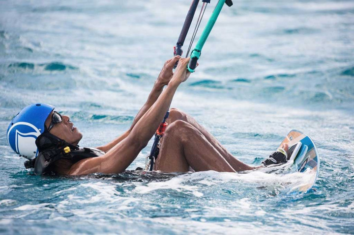 Obama tersenyum di papan speed boat dengan mengenakan helm dan kacamata saat ia mencoba olahraga kitesurfing.