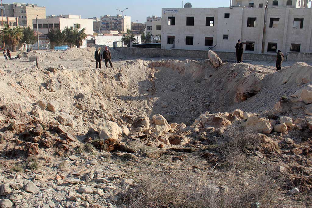 Warga melihat kawah yang ditimbulkan akibat serangan udara di Idlib.
