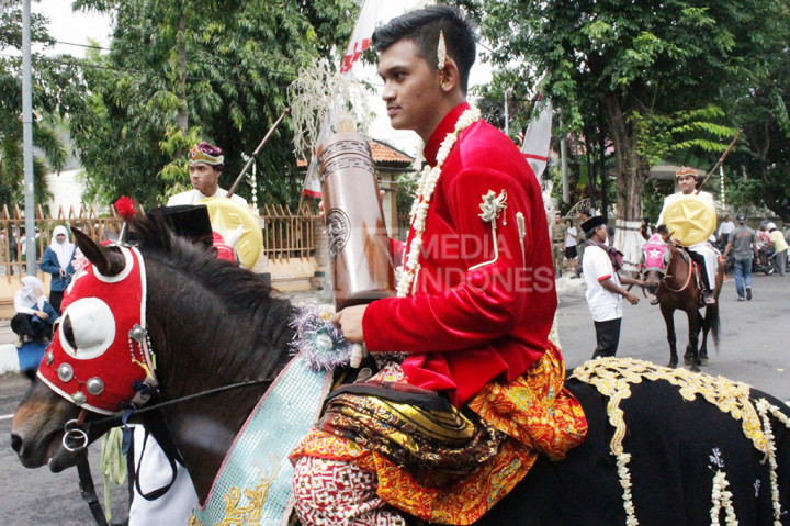 Seorang prajurit berpakaian merah membawa tabung bambu yang berisi pataka Untung Suropati. 