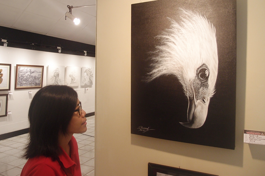 Seorang perempuan memperhatikan sebuah lukisan berjudul 