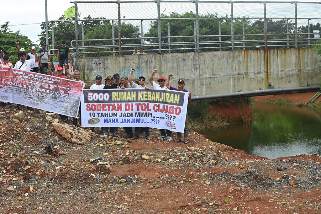 Warga berunjuk rasa membentangkan spanduk kritik terhadap pembangunan Tol Cijago yang berdampak banjir di lokasi proyek.