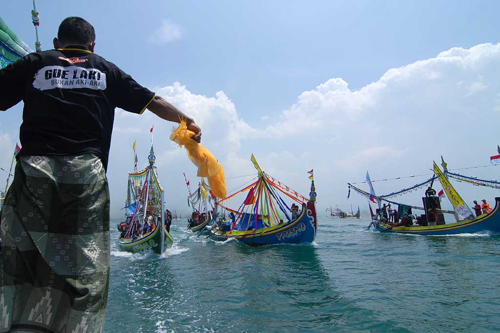Seorang nelayan memberikan tanda agar parade perahu hias berhenti saat akan melarung sesaji dalam ritual 'Petik Laut'.