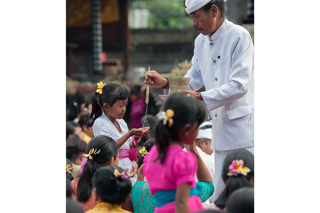 Seorang pemuka agama Hindu memercikkan air suci kepada umat saat persembahyangan di Pura Dalem Kengetan, Ubud.