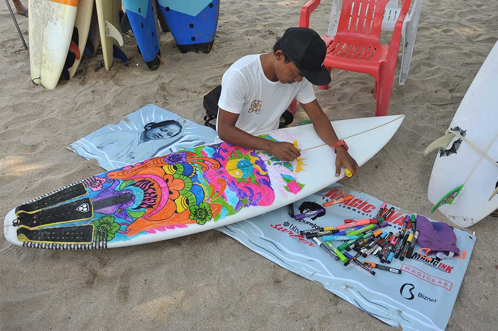 Seorang seniman melukis papan selancar untuk menyambut Hari Kartini 