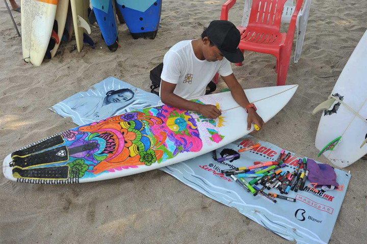 Seorang seniman melukis papan selancar untuk menyambut Hari Kartini 