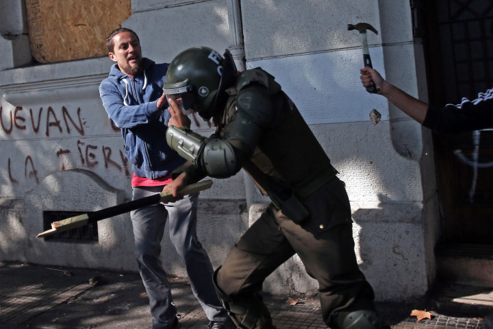 Seorang polisi berusaha menyelamatkan diri dari kepungan buruh yang mencoba memukulnya dengan martil.