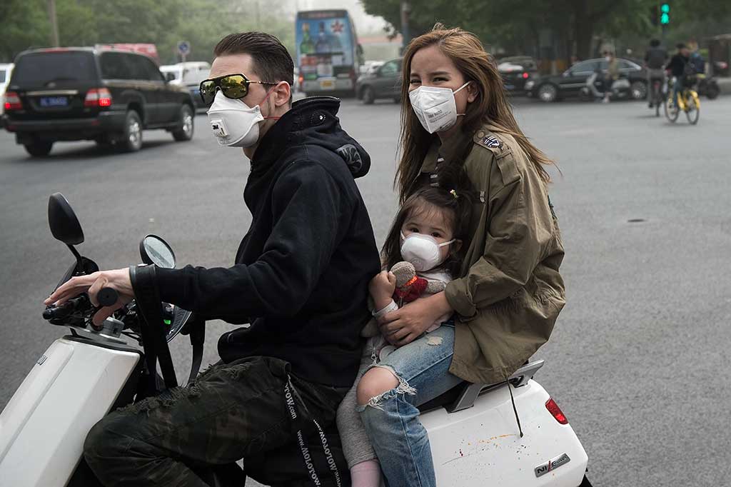 Sepasang suami istri dengan anaknya yang masih balita harus memakai masker saat melaju di jalanan di Beijing.