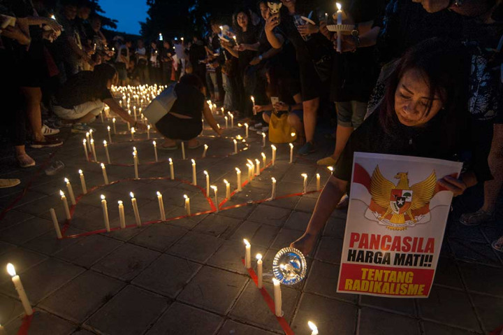Seorang warga menyalakan lilin sambil membawa poster bertuliskan 'Pancasila Harga Mati, Tentang Radikalisme.