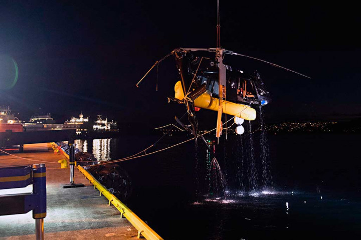 Petugas dibantu alat berat berusaha mengevakuasi sebuah helikopter yang terjun ke laut di dekat pelabuhan Bergen, Norwegia, Kamis (11/5/2017) malam waktu setempat. 