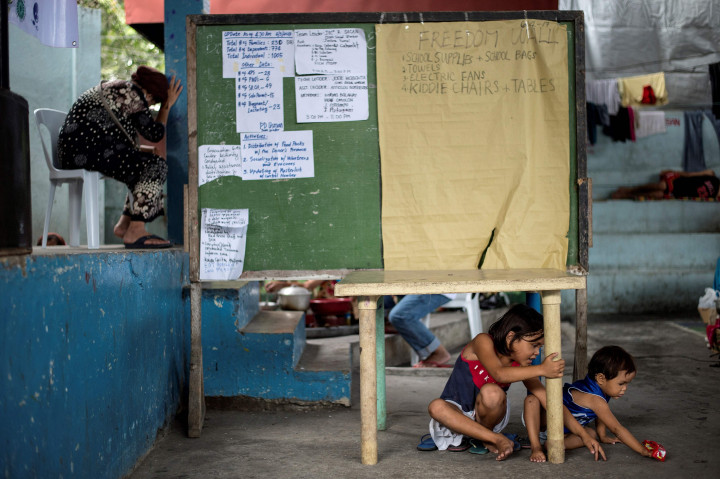 Anak-anak bermain di bawah papan penuh daftar nama warga yang masih dinyatakan hilang oleh keluarganya. 