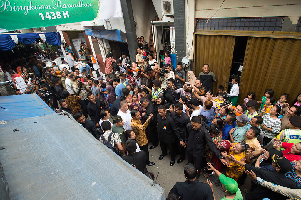 Presiden Joko Widodo (tengah) melambaikan tangan kepada warga yang mengantre pembagian sembako di Jalan Rawa Bebek 2, Jakarta, Selasa (13/6/2017).