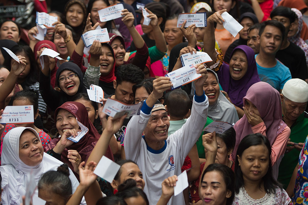 Warga menunjukkan kupon penukaran saat mengantre pembagian sembako.