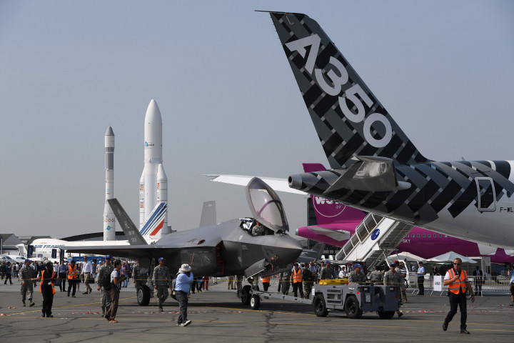 Jet tempur Lockheed Martin F-35 ditarik melintasi runway Bandara Le Bourget. Di latar belakang tampak sosok roket antariksa Arianne dan di depan adalah ekor pesawat penumpang berbadan lebar Airbus A350-1000.  AFP PHOTO / CHRISTOPHE ARCHAMBAULT