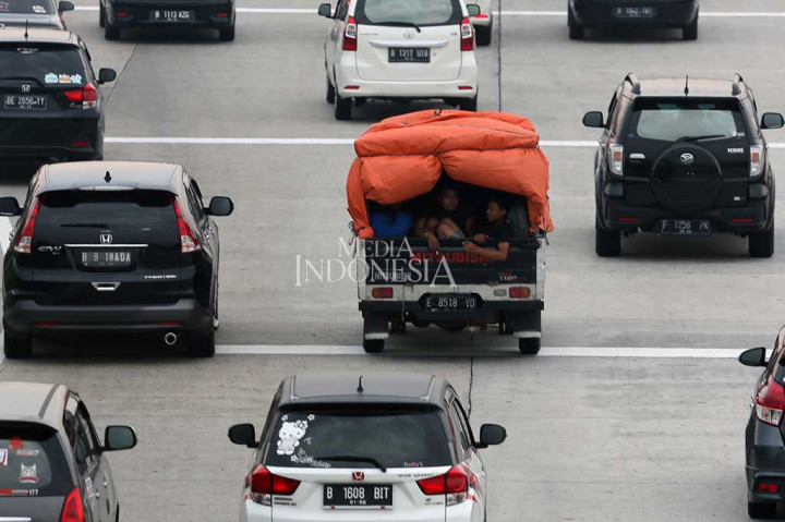 Duduk beratapkan terpal berangka bambu sembari berbagi tempat dengan tumpukan barang bawaan, para pemudik menumpang mobil bak terbuka untuk menuju kampung halaman mereka.