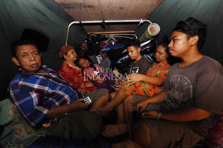 Sebuah keluarga duduk berimpit dan harus berbagi dengan sepeda motor di dalam mobil bak terbuka.