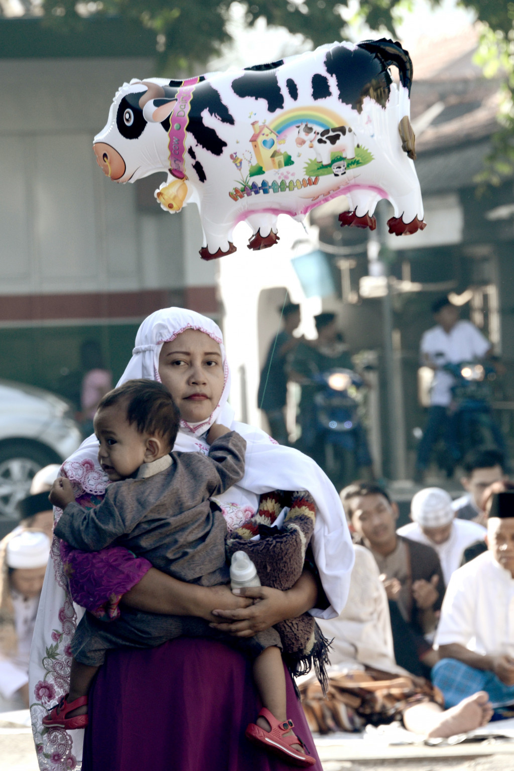 Seorang ibu menggendong putranya yang menggembang balon mainan berbentuk sapi di Tangerang. Di Indonesia, salat Ied adalah bagian dari kemeriahan rangkaian perayaan hari raya Idul Fitri. AFP Photo/Goh Cai Hin