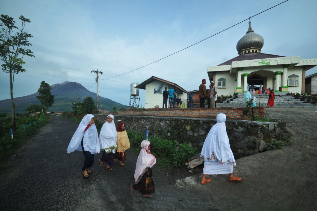 Umat Islam di Karo bersiap menuju sebuah masjid. Gunung Sinabung, Sumatera Utara, nampak di bagian latar belakang. AFP Photo/Gatha Ginting