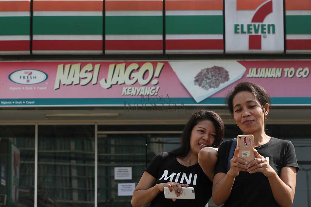 Pengunjung menyempatkan foto dengan latar gerai 7-Eleven yang tutup di kawasan Tugu Tani, Jakarta. 