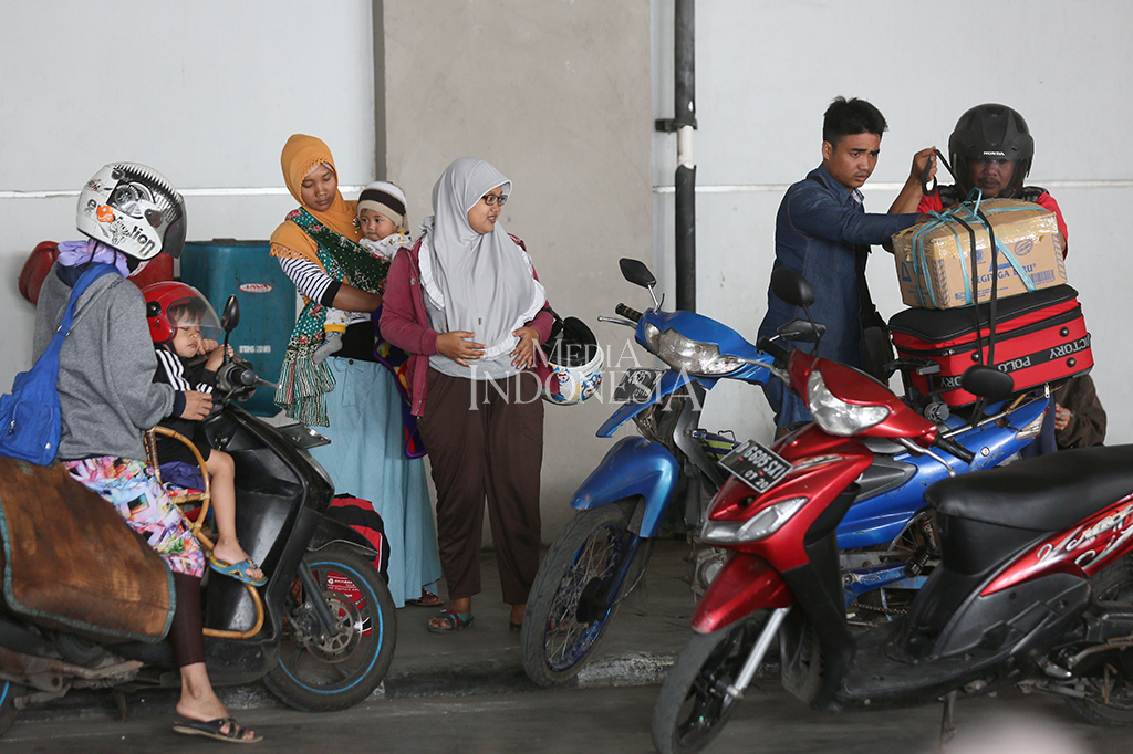 Seorang pemudik sedang merapihkan barang bawaan nya ke atas motor untuk melanjutkan perjalanannya menuju rumah.