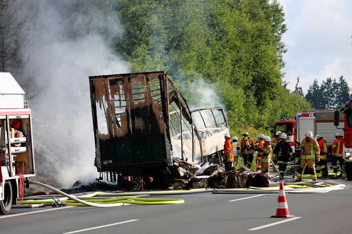 Petugas berusaha memadamkan api di lokasi kecelakaan sebuah bus terbakar tidak lama setelah menabrak truk trailer di ujung kemacetan di jalan raya A9 dekat Muenchberg, Jerman selatan, Senin (3/7/2017) waktu setempat.