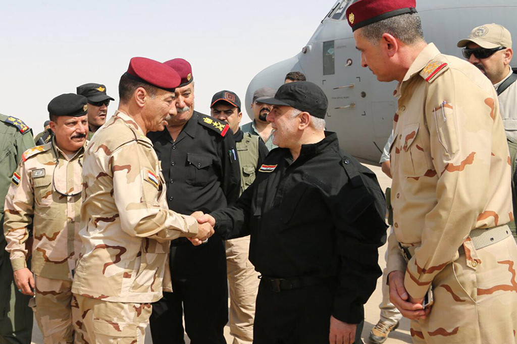 PM Abadi terlihat mengenakan seragam tentara berwara hitam lengkap dengan topi baret, dan menyalami pasukan keamanan yang terdiri dari polisi dan tentara.