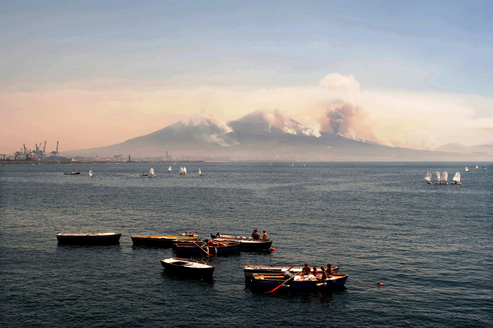 Asap tebal kebakaran hutan terlihat mumbumbung di punggung gunung berapi Vesuvius. Di latar depan adalah perahu dayung para wisawatan yang sedang berjemur.