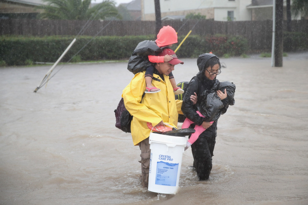 Di bawah guyuran hujan, sepasang suami istri menggendong dua anak balitanya berjalan menembus banjir menuju tempat pengungsian. Banjir diperkirakan belum akan surut dalam waktu dekat. Scott Olson/Getty Images/AFP