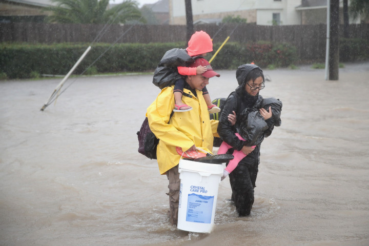 Di bawah guyuran hujan, sepasang suami istri menggendong dua anak balitanya berjalan menembus banjir menuju tempat pengungsian. Banjir diperkirakan belum akan surut dalam waktu dekat. Scott Olson/Getty Images/AFP