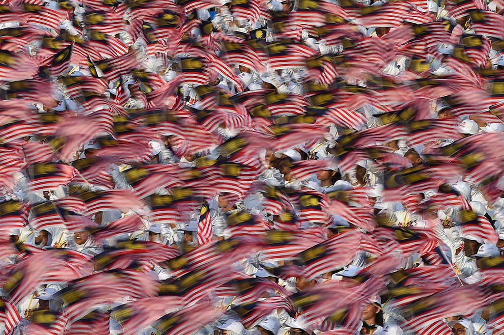 Anak-anak sekolah berparade sambil melambaikan bendera nasional Malaysia. 