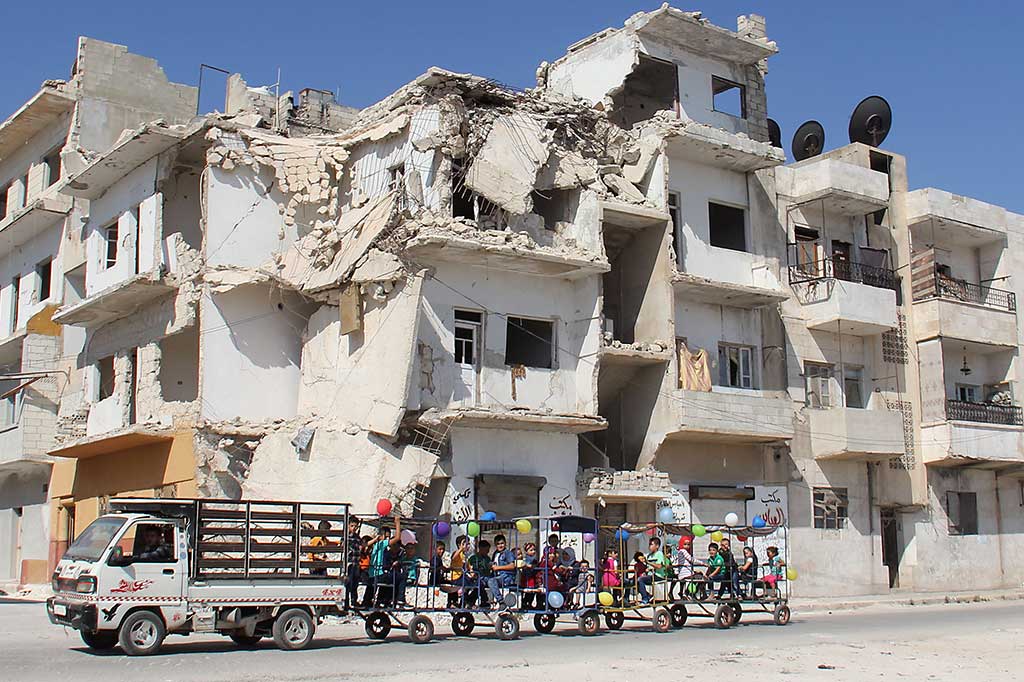 Anak-anak menaiki odong-odong dengan latar belakang bangunan yang hancur akibat konflik berkepanjangan di Kota Idlib. AFP/Omar Haj Kadour