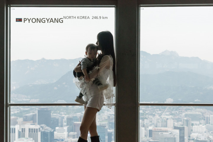 Seorang ibu muda menggendong bayinya berpose di di puncak Namsan Tower, Seoul. Jaraknya dari Pyongyang yang berada di balik bukit yang nampak di latar belakangnya hanya 246,9 kilometer. AFP Photo/Ed Jones