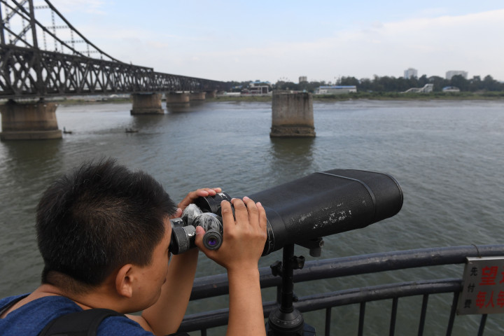 Seorang turis di daerah wisata Jembatan Patah, Liaoning, Tiongkok, mengarahkan teropongnya ke wilayah Korea Utara yang berada di seberangnya. Jembatan penghubungkan Dandong, Tiongkok, dengan Sinuiju, Korut, yang dipisahkan Sungai Yalu ini dibom oleh militer AS dalam Perang Korea. AFP Photo/Greg Baker