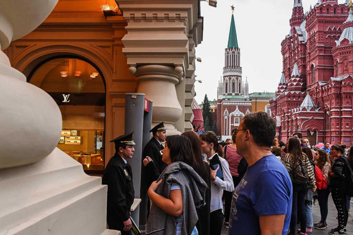 Petugas keamanan berjaga-jaga di depan pintu masuk, sementara pengunjung menunggu di luar Supermarket GUM di dekat Lapangan Merah, Moskow. Lebih dari 30 lokasi penting di Moskow untuk sementara dikosongkan setelah ancaman bom lewat telepon anonim. AFP/Vasily Maximov